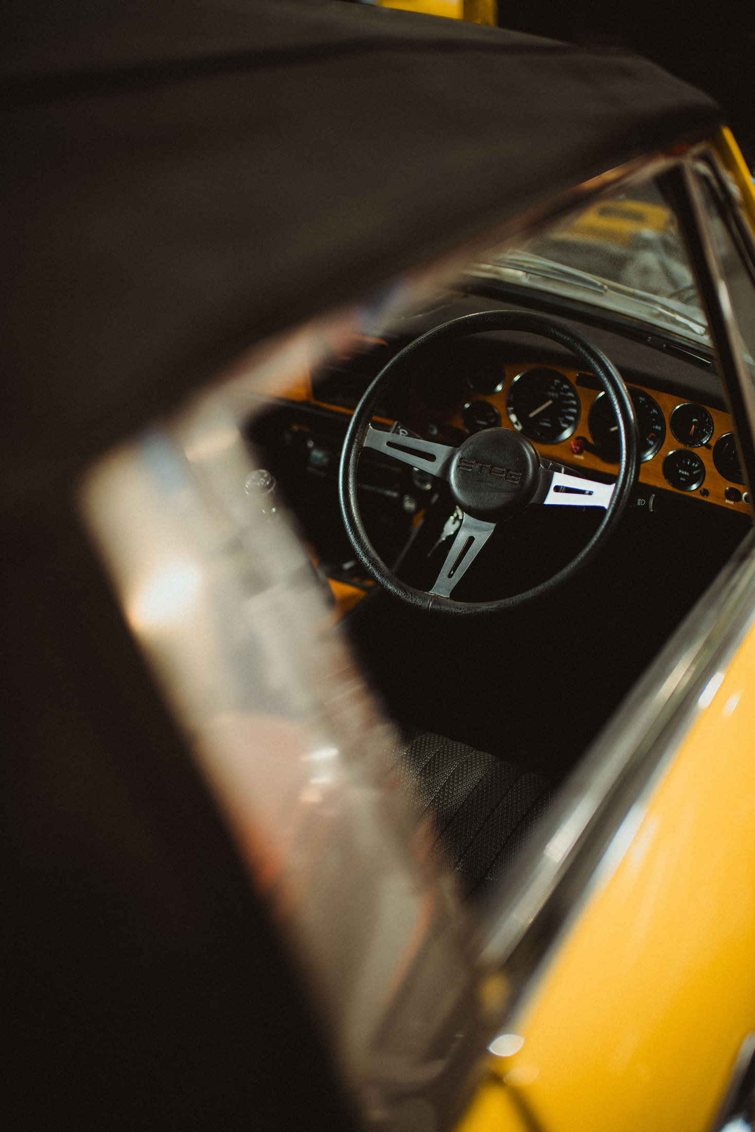 Dashboard and steering wheel of a yellow convertible, shot through the window