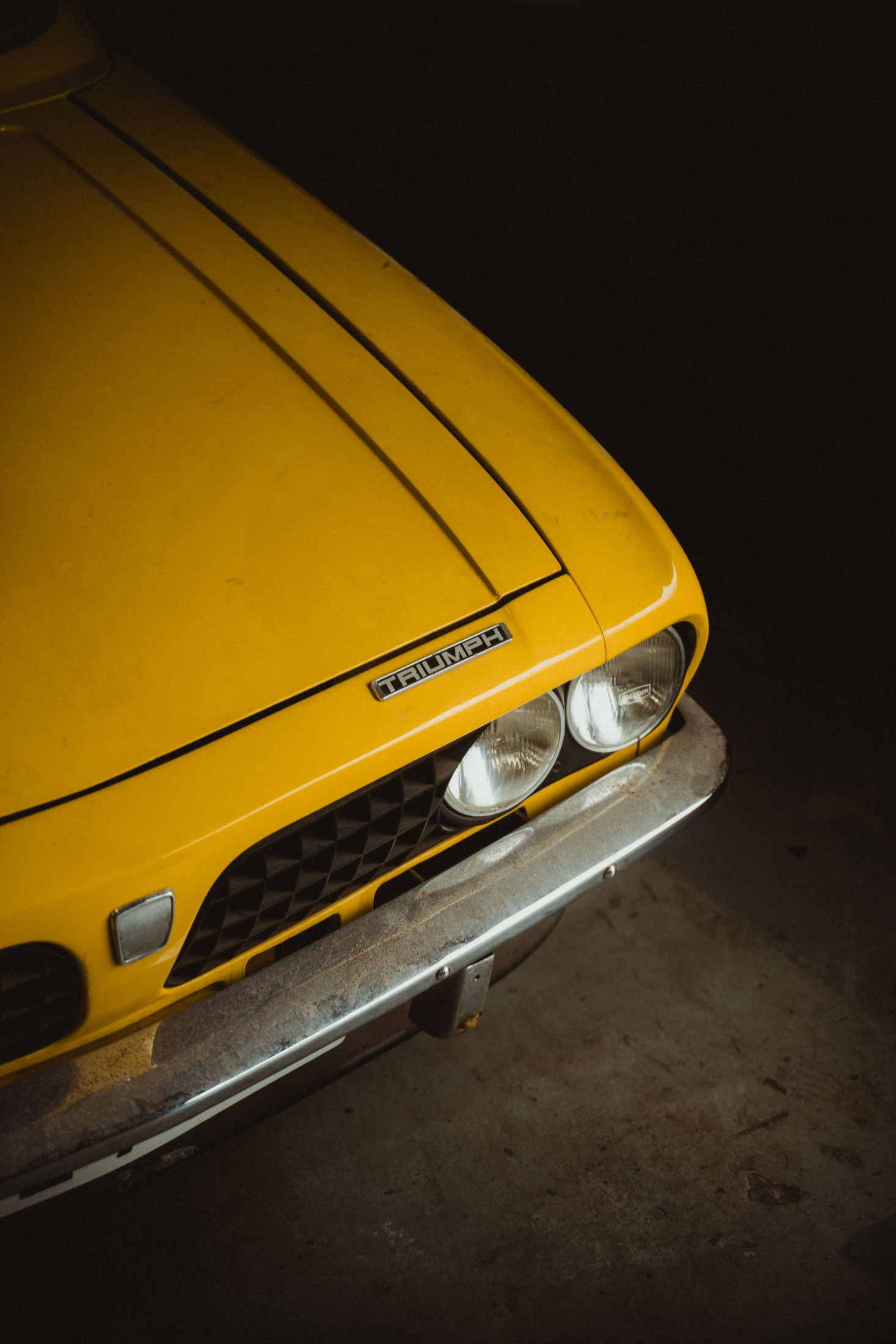 Front of a yellow classic car in a dark workshop